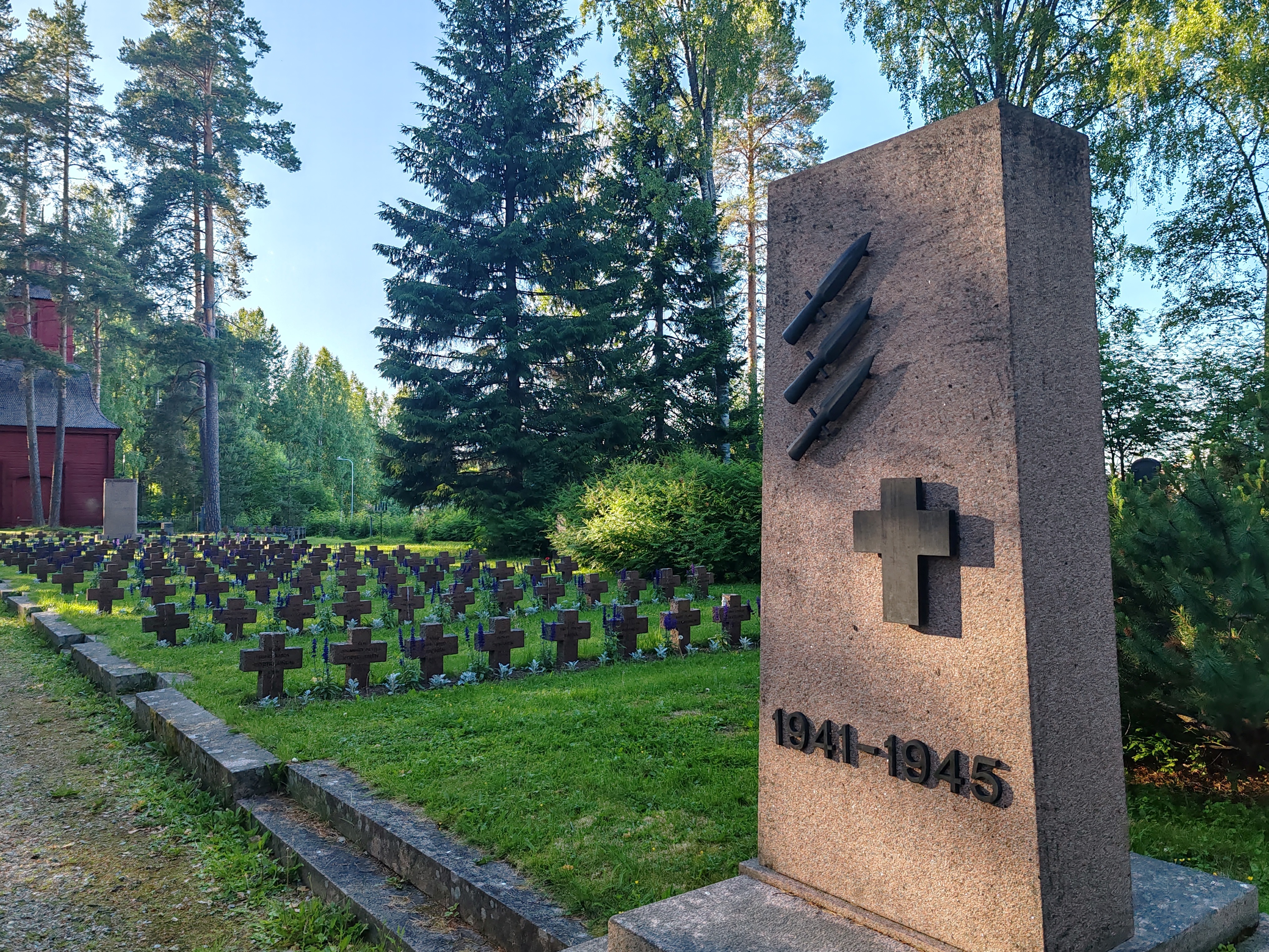 Sankarihautausmaa Kuvassa hautamuistomerkkejä ja vanha tapuli siintää taustalla.