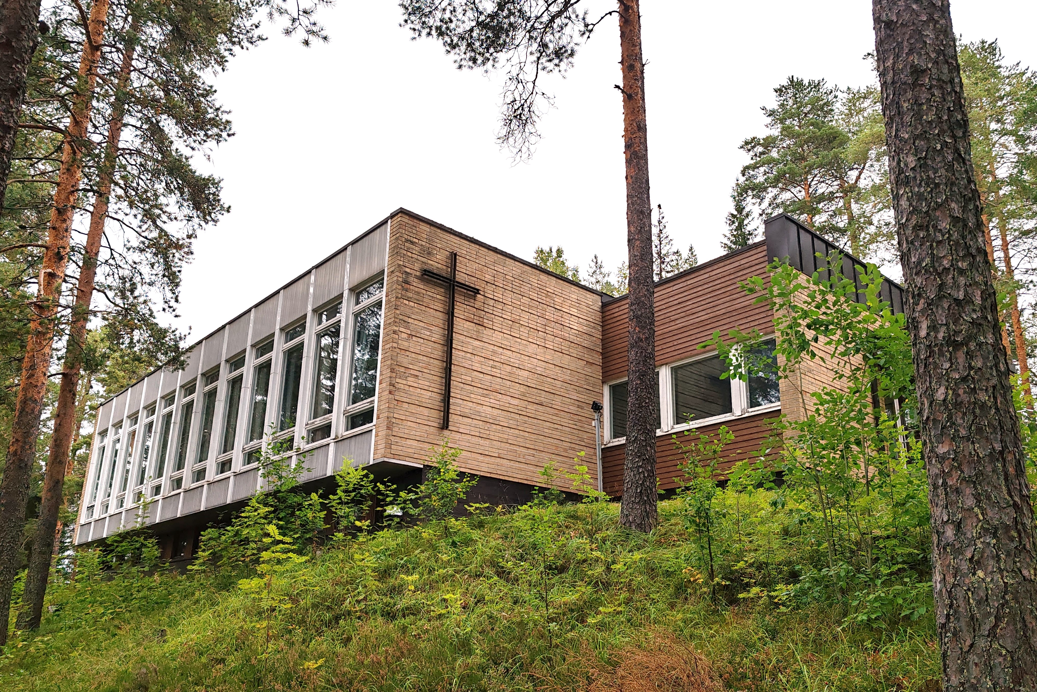 Valtimon seurakuntatalo Kuvassa tiilinen rakennus puiden keskellä eli Valtimon seurakuntatalo.
